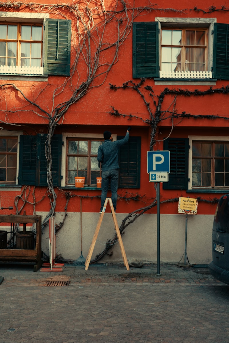 Painter on a Ladder Repainting a Red Building Exterior
